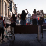 Protesters holding up Black Lives Matter signs on Lake Street at Hennepin Avenue with barricades in place. Protesters have been protesting the June 3rd law enforcement killing of Winston Smith and the June 13th killing of Deona Marie.Marie was killed when Nicholas Kraus drove his vehicle into those protesting the killing of Smith.