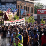 Protesters carrying signs that read "This is a Revolt Against Racism! Stop the War on Black America!" while marching through the streets of Uptown Minneapolis.Protesters have been marching since the June 3rd law enforcement shooting death of Winston Smith and the June 13th killing of protester Deona Marie. Marie was killed when Nicholas Kraus drove his vehicle into those protesting the killing of Smith.