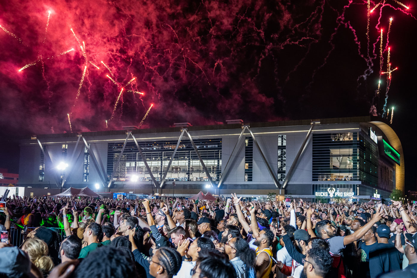 Fireworks explode over Fiserv Forum in Milwaukee, celebrating the Milwaukee Bucks' 2021 NBA Championship win. A large crowd gathers in the Deer District for the event.