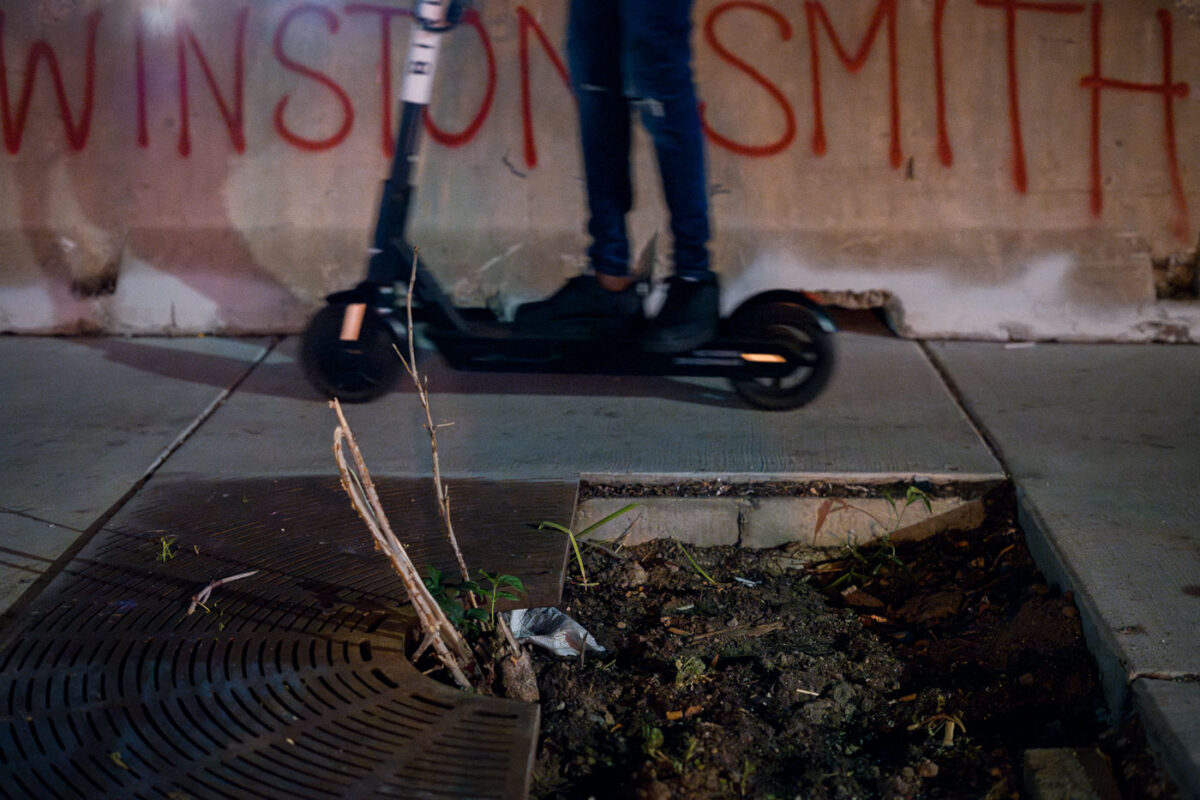 A protester rides a Scooter across barricades that read "Winston Smith" in Uptown Minneapolis on Lake Street.