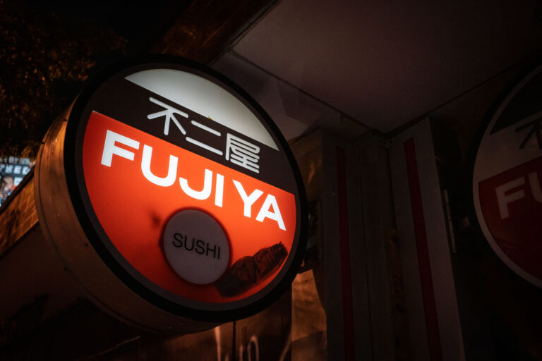 Fujiya Sushi Restaurant Sign at Night 4 The illuminated Fujiya Sushi restaurant sign, featuring English and Japanese text, is visible at night. This sign serves to attract customers to the establishment.