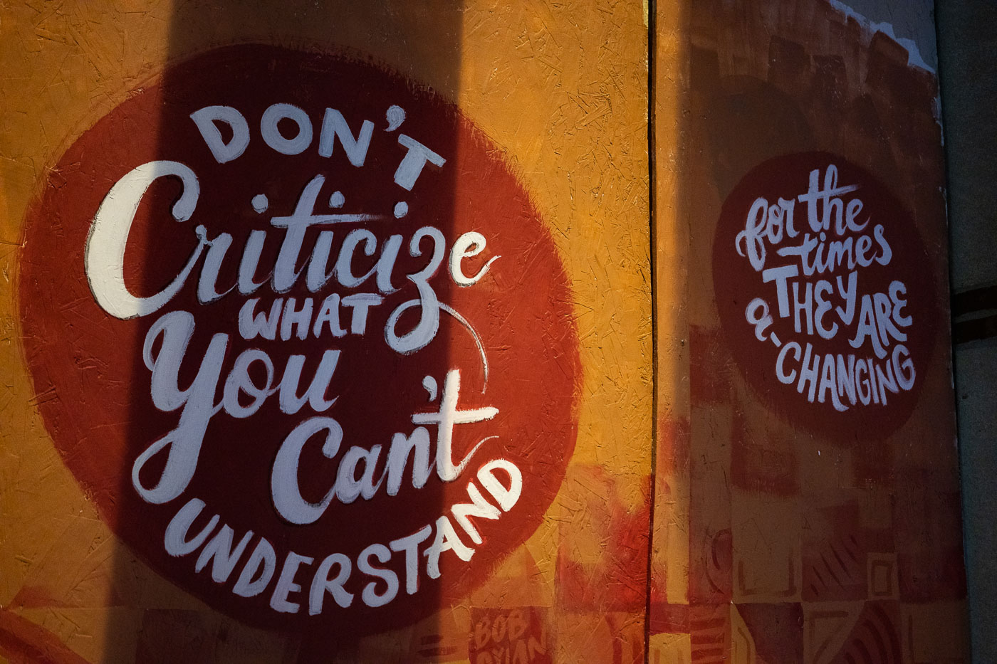 Mural with Bob Dylan quote "Don't criticize what you can't understand" and "for the times & they are changing" painted on an orange and brown textured surface.