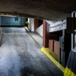 A lower-level vehicle ramp inside the Northstar Center parking garage in downtown Minneapolis. Built as part of the original 1960s mixed-use complex, the garage reflects the era’s push to accommodate growing automobile traffic in the central business district. Its narrow lanes, low ceilings, and concrete-banded structure are typical of mid-century urban parking facilities designed to integrate directly with office towers and the city’s emerging skyway network. Despite renovations to portions of the complex above, much of the garage retains its original utilitarian character, serving daily commuters and visitors accessing nearby government buildings, hotels, and transit connections.