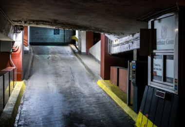 A lower-level vehicle ramp inside the Northstar Center parking garage in downtown Minneapolis. Built as part of the original 1960s mixed-use complex, the garage reflects the era’s push to accommodate growing automobile traffic in the central business district. Its narrow lanes, low ceilings, and concrete-banded structure are typical of mid-century urban parking facilities designed to integrate directly with office towers and the city’s emerging skyway network. Despite renovations to portions of the complex above, much of the garage retains its original utilitarian character, serving daily commuters and visitors accessing nearby government buildings, hotels, and transit connections.