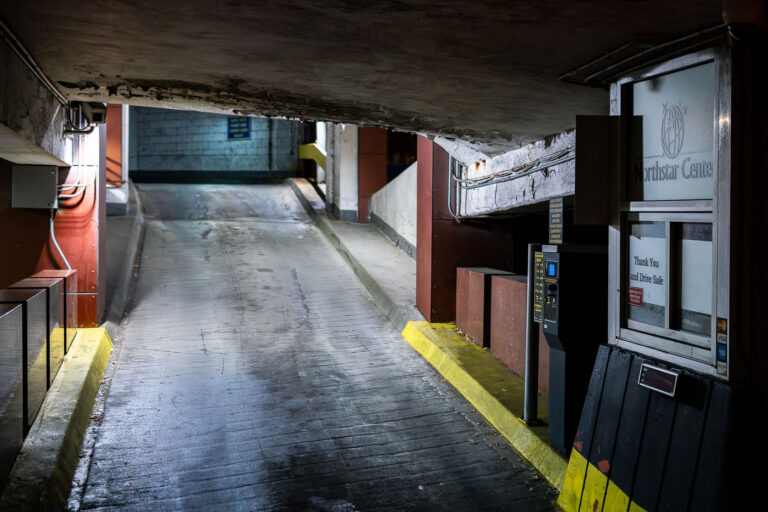 Northstar Center Parking Garage Ramp, Minneapolis 1 A lower-level vehicle ramp inside the Northstar Center parking garage in downtown Minneapolis. Built as part of the original 1960s mixed-use complex, the garage reflects the era’s push to accommodate growing automobile traffic in the central business district. Its narrow lanes, low ceilings, and concrete-banded structure are typical of mid-century urban parking facilities designed to integrate directly with office towers and the city’s emerging skyway network. Despite renovations to portions of the complex above, much of the garage retains its original utilitarian character, serving daily commuters and visitors accessing nearby government buildings, hotels, and transit connections.