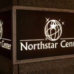 A backlit sign marks the entrance to Northstar Center, a three-building complex that has been a fixture of downtown Minneapolis since the early 1960s. Developed during a period of major postwar urban renewal, the complex originally combined office space, a hotel, retail, and skyway connections under one coordinated design—an early example of the mixed-use development model that would later define much of the downtown core. Today, the Northstar Center remains tied into the city’s extensive skyway system and continues to serve as a key pedestrian link between the central business district and nearby transit corridors.