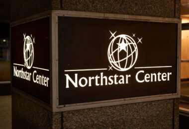 A backlit sign marks the entrance to Northstar Center, a three-building complex that has been a fixture of downtown Minneapolis since the early 1960s. Developed during a period of major postwar urban renewal, the complex originally combined office space, a hotel, retail, and skyway connections under one coordinated design—an early example of the mixed-use development model that would later define much of the downtown core. Today, the Northstar Center remains tied into the city’s extensive skyway system and continues to serve as a key pedestrian link between the central business district and nearby transit corridors.