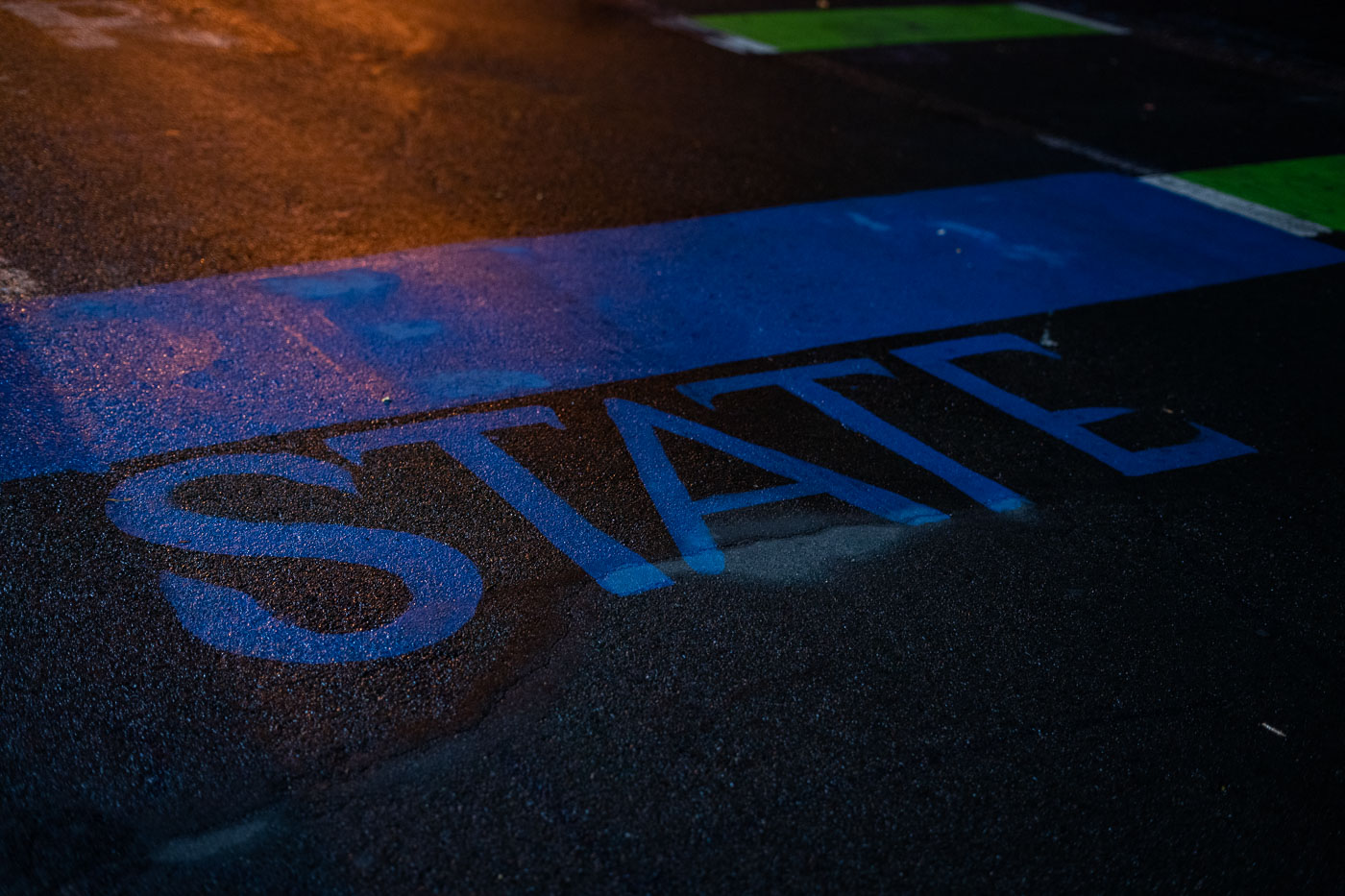 Blue painted word STATE on asphalt at night, likely marking a state line or jurisdictional boundary.