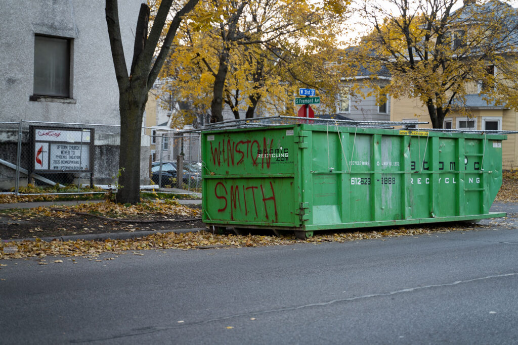 A dumpster with "Winston Smith" written on it. Smith was shot and killed by a federal task force on top of the parking garage across the street.