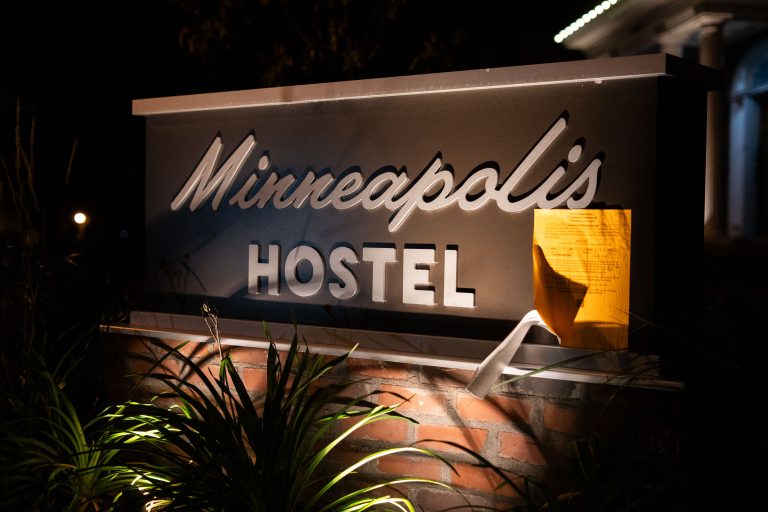 Minneapolis Hostel Sign at Night 1 The illuminated Minneapolis Hostel sign is visible at night, marking a location for affordable lodging in the city.