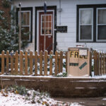 A small handmade “Free Stuff Inside” cabinet sits beside a picket fence in a residential Minneapolis neighborhood, offering passersby clothing, household items, and other essentials at no cost. These volunteer-maintained boxes—modeled loosely after Little Free Pantries and similar mutual-aid projects—became common across the city in recent years as neighbors looked for practical ways to support one another. This particular cabinet shows signs of winter use, with a thin layer of snow on the ground and along the fence, emphasizing the year-round effort by residents to keep shared resources accessible.

The rise of these informal exchange boxes reflects a broader culture of grassroots support systems that grew during the pandemic and the 2020 unrest. Neighbors created hyper-local networks for food, winter gear, and daily necessities, often improvising with whatever materials they had. Even a small cabinet like this served as a reliable touchpoint for people needing gloves, toiletries, or household supplies, helping strengthen the sense of community resilience in the city’s residential blocks.