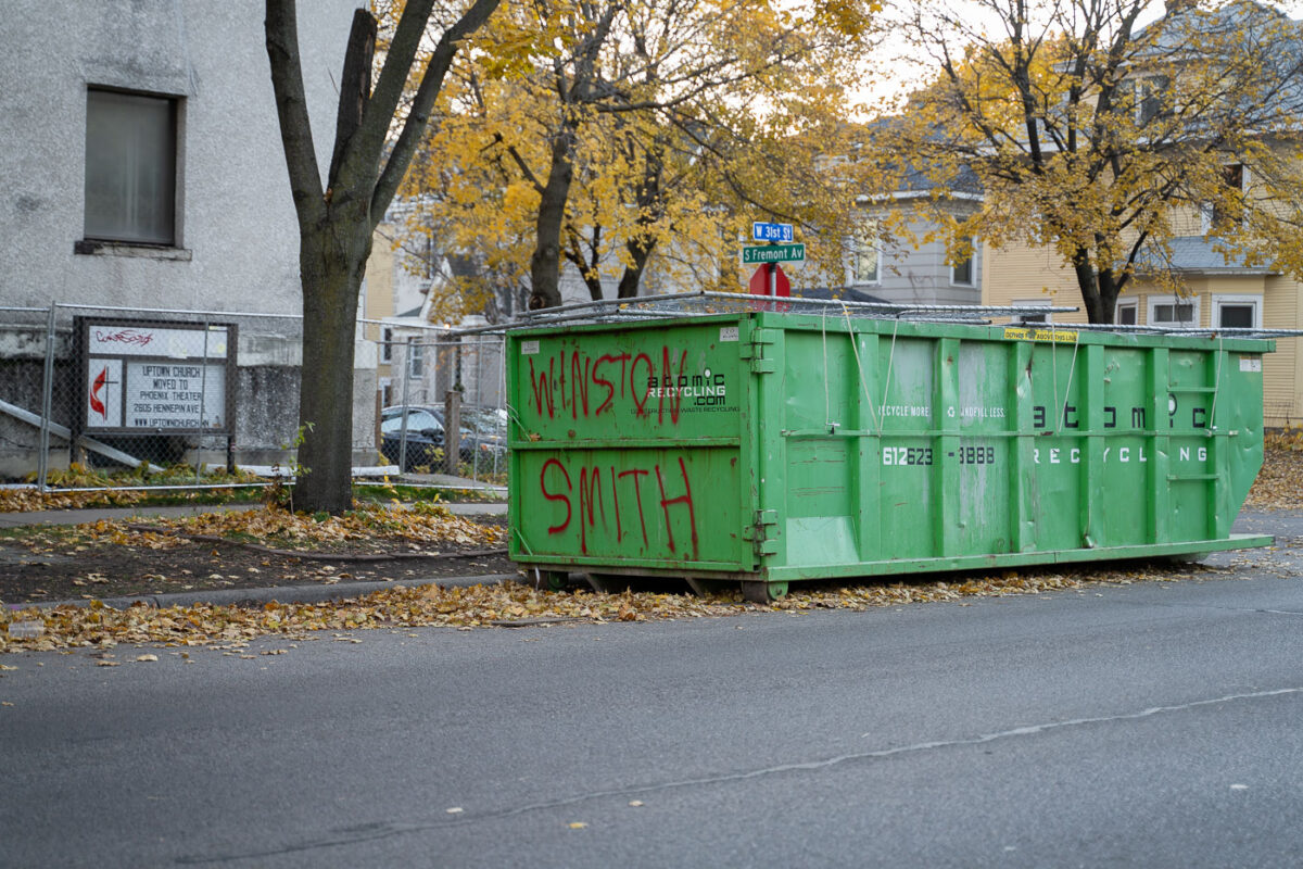 A dumpster with "Winston Smith" written on it. Smith was shot and killed by a federal task force on top of the parking garage across the street.