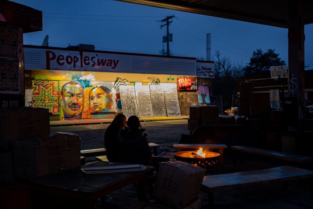 Two people sit around the fire at George Floyd Square in December 2021.