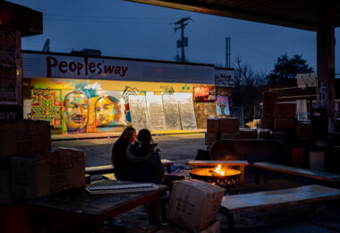 Two people sit around the fire at George Floyd Square in December 2021.