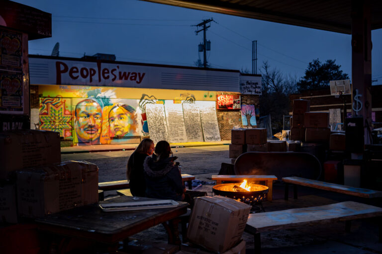 Campfire at George Floyd Square December 2021 2 Two people sit around the fire at George Floyd Square in December 2021.