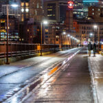 A couple holds hands walking over the Stone Arch Bridge in downtown Minneapolis.