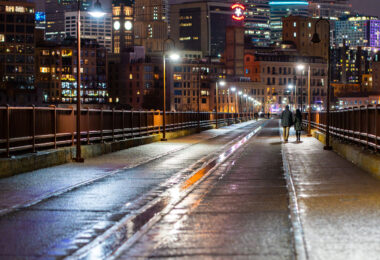 A couple holds hands walking over the Stone Arch Bridge in downtown Minneapolis.