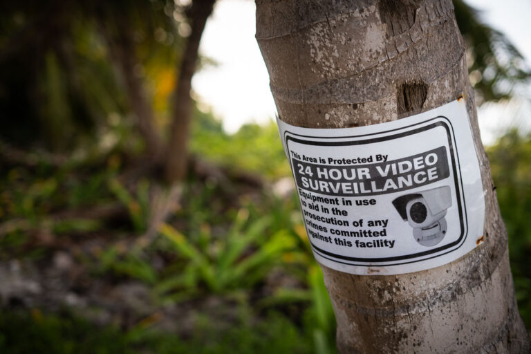 A printed notice affixed to a coconut palm on Ambergris Caye warns of 24-hour video surveillance—an increasingly common sight around resorts and beach properties as tourism expands. Such measures reflect efforts by local authorities and businesses to balance safety, privacy, and preservation amid the island’s rapid growth and environmental pressures.