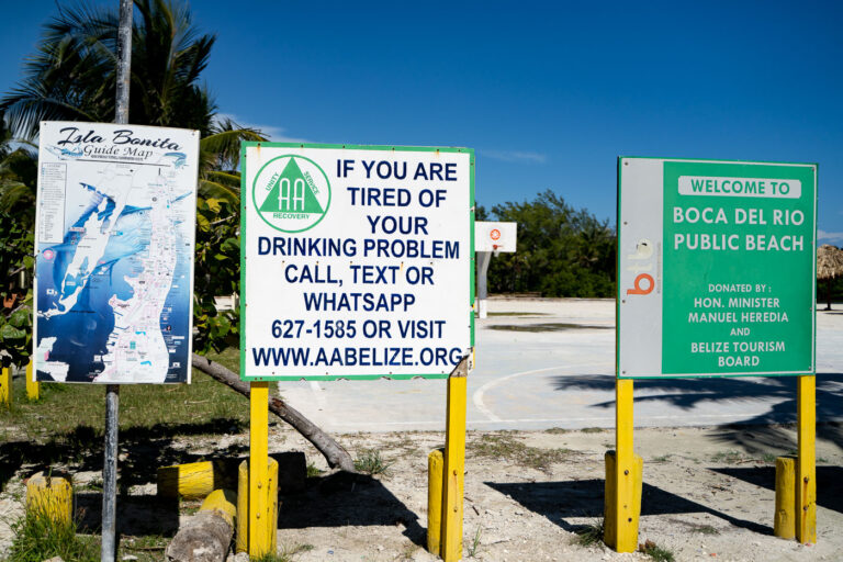 AA Belize Signs 1 At the entrance to Boca Del Rio Public Beach, north of central San Pedro, community signs mark local initiatives including AA recovery outreach and tourism development sponsored by the Belize Tourism Board. Boca Del Rio, meaning “mouth of the river,” is one of the few remaining public-access beaches on Ambergris Caye, frequently used for volleyball, community events, and informal recreation by residents.