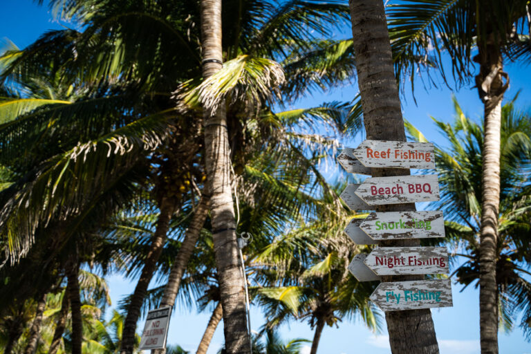 Ambergris Caye signage on a tree 2 A hand-painted wooden sign in San Pedro lists classic Caribbean pastimes—reef fishing, snorkeling, beach barbecues, and fly fishing—reflecting the local economy’s dependence on marine tourism. The area’s surrounding waters are protected as part of the Hol Chan Marine Reserve, a major conservation zone established in 1987 to preserve coral reef and mangrove ecosystems along the Belize Barrier Reef.
