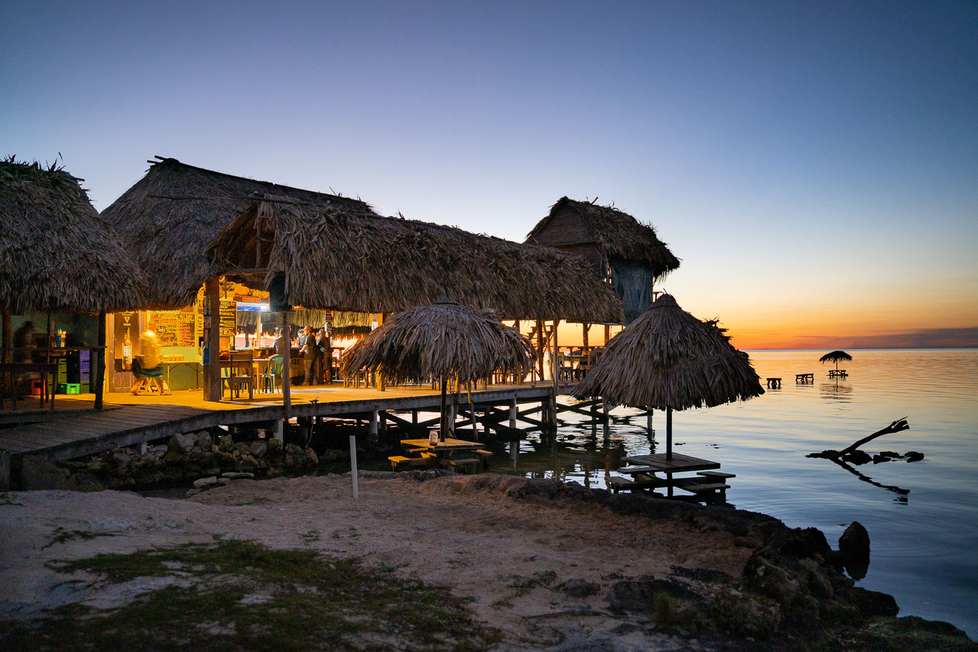 The Blue Bayou Bar and Grill, with thatched roofs and wooden construction, is located on Secret Beach, Ambergris Caye, Belize, at dusk.
