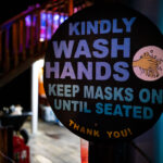 COVID-19 sign in Belize 2 "Kindly wash hands keep masks on until seated Thank you" sign outside a restaurant in San Pedro, Belize.