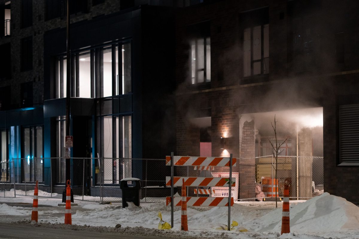 Steam rises from a cordoned construction site in downtown Minneapolis at night.