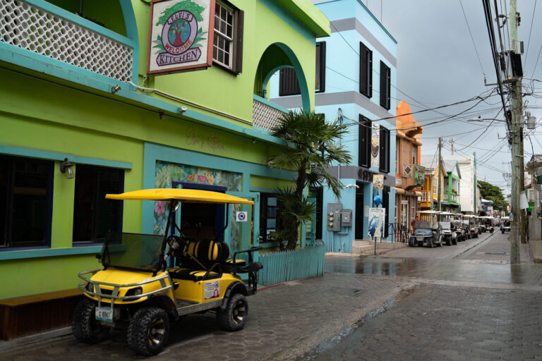 Elvi's Kitchen and Golf Carts on Cobblestone Street, San Pedro, Belize 2 Golf carts line a cobblestone street in San Pedro, Belize, in front of Elvi's Kitchen restaurant under an overcast sky.