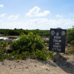 A weathered sign reading “Keep Calm and Don’t Litter” stands at the edge of a mangrove wetland on Ambergris Caye, Belize. These coastal mangrove ecosystems play a critical role in protecting shorelines, supporting marine life, and filtering water, making local anti-littering efforts especially important. The sign, posted by community and conservation groups, reflects ongoing grassroots work to preserve the island’s fragile environment amid steady development and tourism growth.