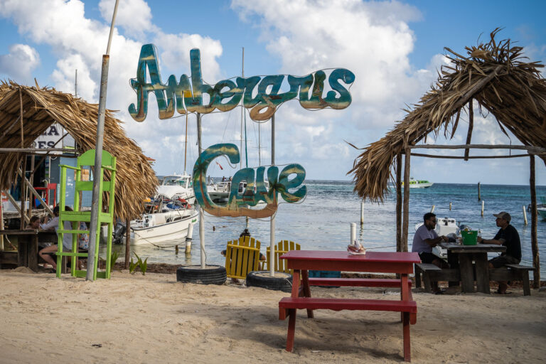 Lunch at Ambergris Caye 4 A casual seaside café on the shores of Ambergris Caye, where wooden signs, thatched palapas, and docked boats convey the island’s relaxed atmosphere. Once a hub for coconut plantations and fishing, Ambergris Caye now thrives on tourism centered on snorkeling, diving, and marine preservation. The area’s name dates back to the colonial era, when “ambergris”—a waxy substance from sperm whales—was a valuable export.