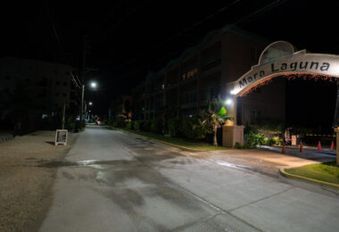 Mara Laguna Resort illuminated along the main north road in San Pedro, Ambergris Caye. The complex sits just across from the lagoon side of the island, a short distance from the town center, and is known for its residential condos and easy access to both the waterfront and nearby businesses. This nighttime view highlights the quiet stretch of road leading past the entrance, a scene typical of the calmer hours on the north side of the island.