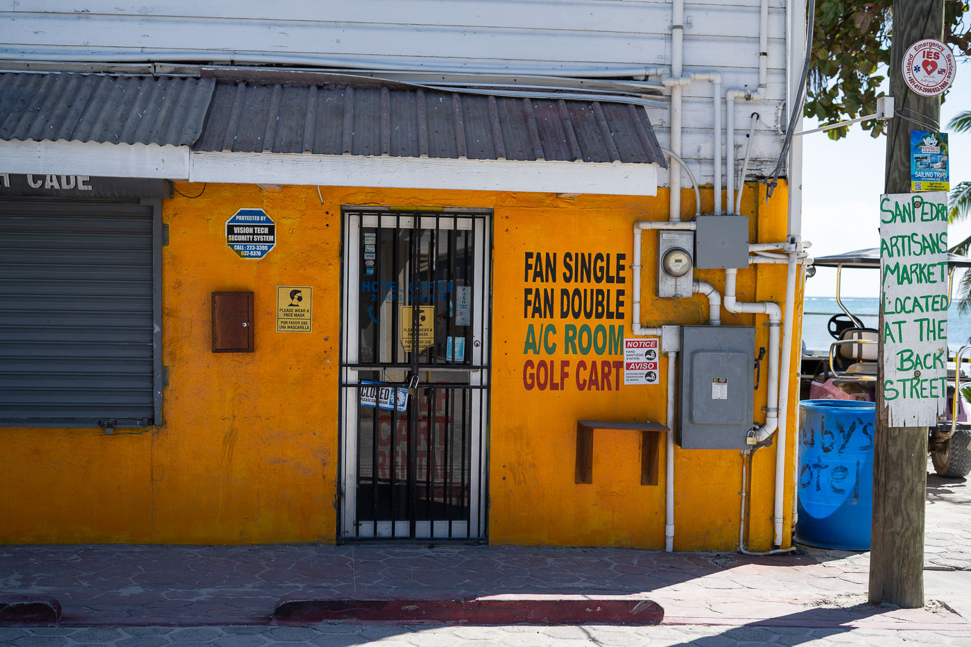 San Pedro, Ambergris Caye: A motel offers A/C rooms and golf cart rentals, with a sign indicating the nearby San Pedro Artisans Market.