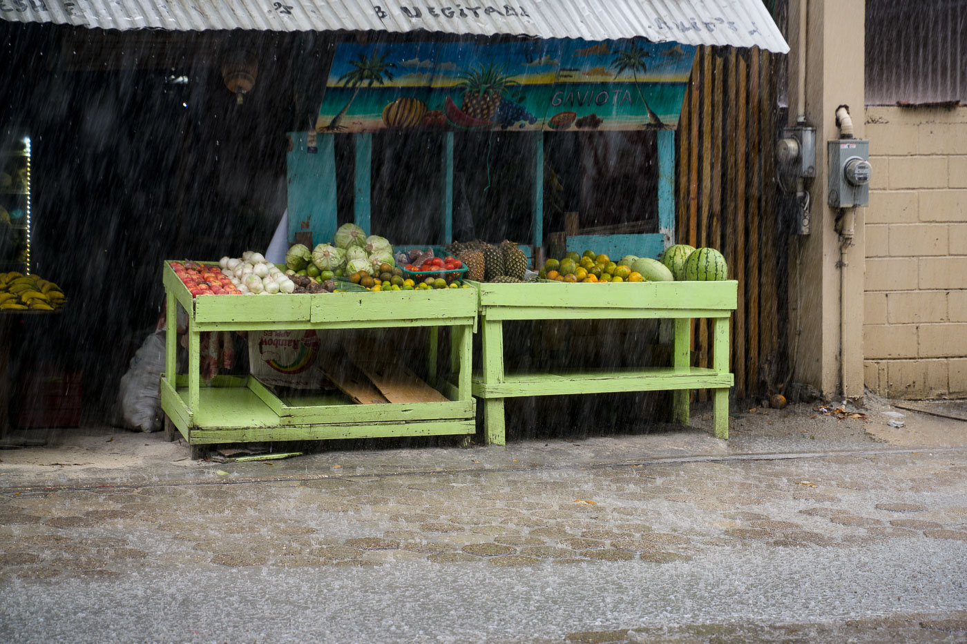 A fruit stand at San Pedro Market on Ambergris Caye, Belize, displays produce during a rain shower. The market is a vital community gathering place.