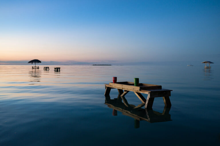Secret Beach, Ambergris Caye, Belize: Dusk Over Water 2 Dusk at Secret Beach, Ambergris Caye, Belize. Submerged wooden structures and thatched umbrellas indicate a developed area for coastal enjoyment.