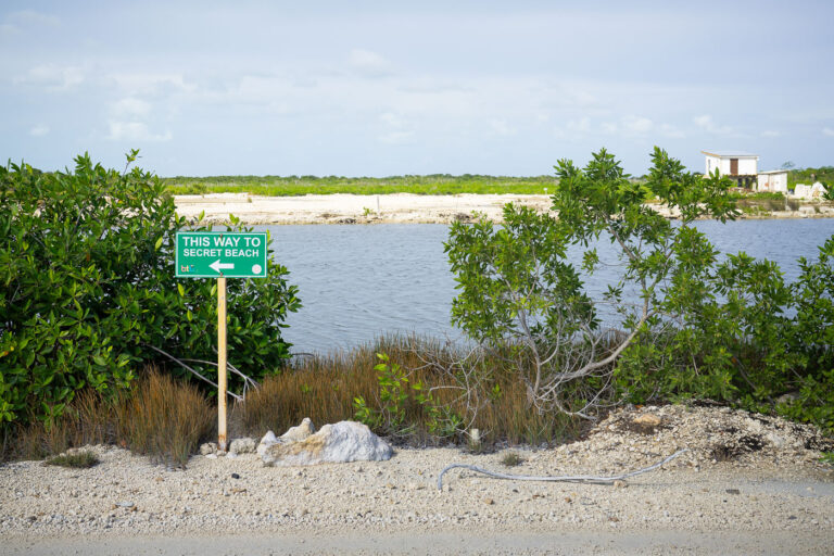 Sign to Secret Beach on Ambergris Caye 4 A green Belize Tourism Board sign points the way to Secret Beach, one of Ambergris Caye’s most popular yet once-remote spots on the island’s western shore. Accessible only by unpaved roads until recent years, Secret Beach has transformed into a lively tourist area lined with bars and piers—symbolizing the island’s evolving relationship between secluded natural beauty and commercial development.