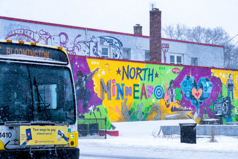 North Minneapolis Mural and Metro Bus in Snowfall 2 A Metro Transit bus passes a vibrant mural in North Minneapolis, Minnesota, during a winter snowfall. The "NORTH MINNEAPOLIS" mural, created in response to the 2020 Minneapolis Uprising, features diverse imagery and text reflecting community identity and resilience. This artwork serves as a significant public statement within the neighborhood. The presence of the bus, a vital public service, highlights the continued operation of transit systems even in inclement weather.