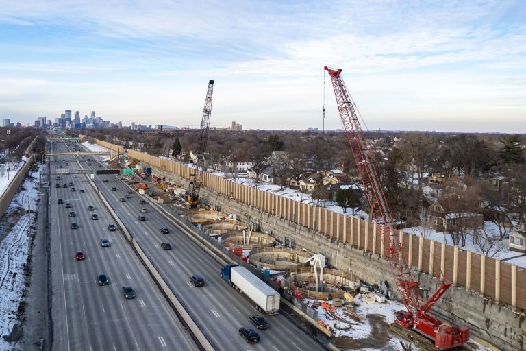 Cranes Over I-35W Stormwater Storage Facility, Minneapolis Skyline Beyond 3 Interstate 35W stormwater storage tunnel construction with cranes and concrete wall barrier alongside active highway.