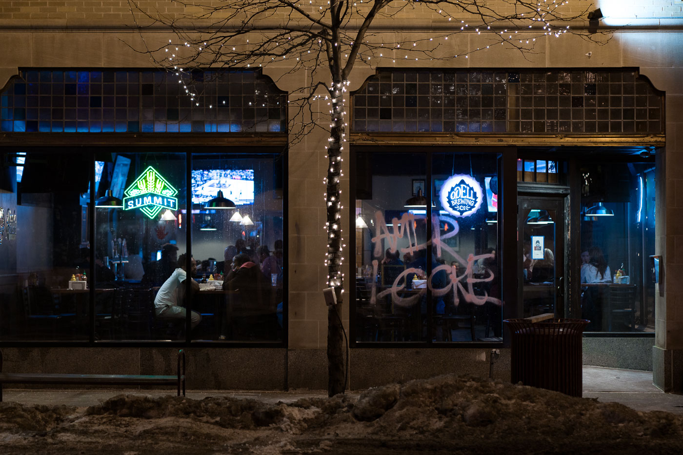 Graffiti reading "AMIR LOCKE" is spray-painted on the window of the Odell Brewing Cafe in Minneapolis's Uptown neighborhood. This act of vandalism occurred on February 2, 2022, the same day Amir Locke was killed by Minneapolis police officers during a no-knock warrant execution. The graffiti serves as a public memorial and a statement of protest against the police killing, appearing in the aftermath of a march where participants chanted "Say His Name! Amir Locke!" as they moved through the commercial corridor of Lake Street.