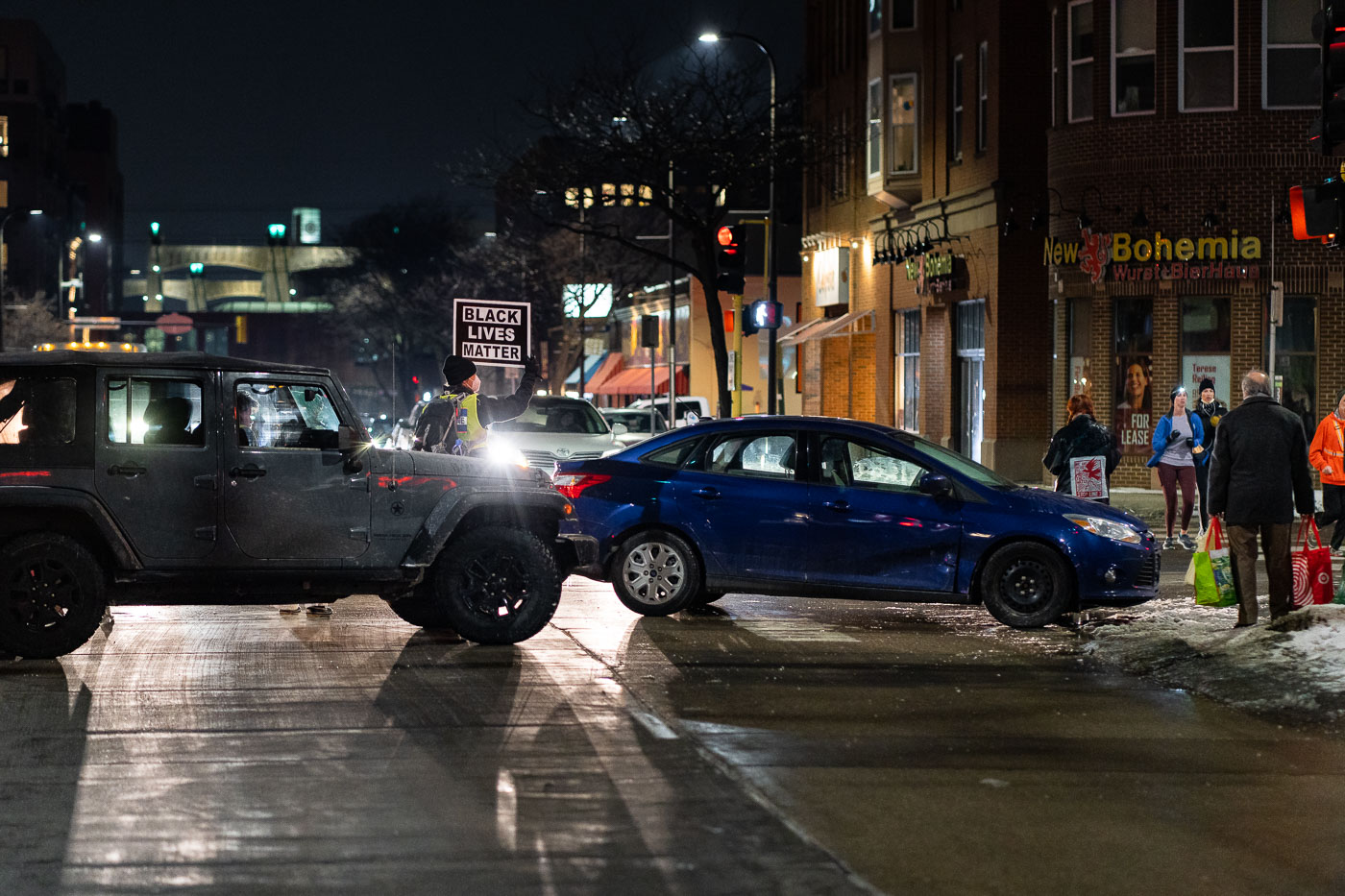 On February 4, 2022, protesters gathered outside the Minneapolis Mayor's residence to demand justice for Amir Locke, who was killed by police earlier that day. The protest, organized by the Black Lives Matter movement, saw participants, including many young people, voicing demands for accountability and systemic change in policing. The "New Bohemia Wurst + BierHaus" sign is visible on the building in the background, indicating the location in Minneapolis.