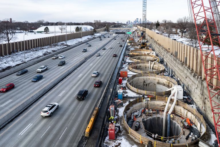 Storage Shafts Beside I-35W Traffic, Minneapolis Skyline Beyond 2 Interstate 35W stormwater storage tunnel construction site with circular concrete sections and active traffic above.