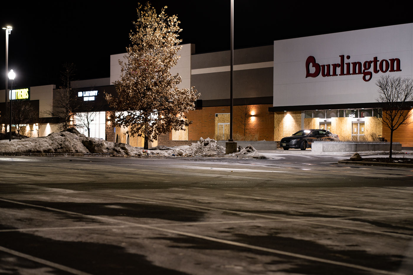 The Burlington store on Lake Street in Minneapolis is boarded up at night, a measure taken in response to property damage and looting that occurred during the Minneapolis Uprising in 2020. The plywood covering the storefront indicates a temporary security measure implemented to protect the business from further vandalism. This event highlighted the vulnerability of commercial areas during periods of civil unrest and the subsequent impact on local economies.