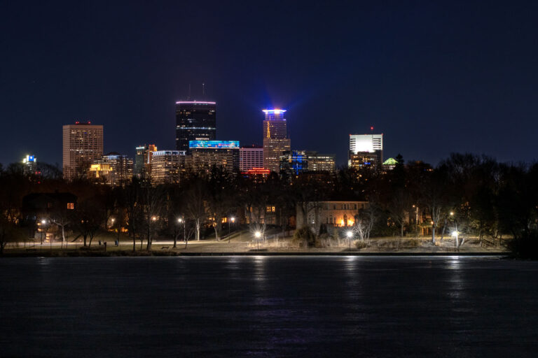 The Minneapolis skyline is visible at night from the frozen surface of Lake of the Isles, a prominent feature of the city's Chain of Lakes park system. This vantage point offers a view of the downtown commercial district, showcasing the development of its architecture and economic activity. Lake of the Isles, established in the late 19th century, serves as a vital green space within the urban environment, providing areas for public use and contributing to the city's character.