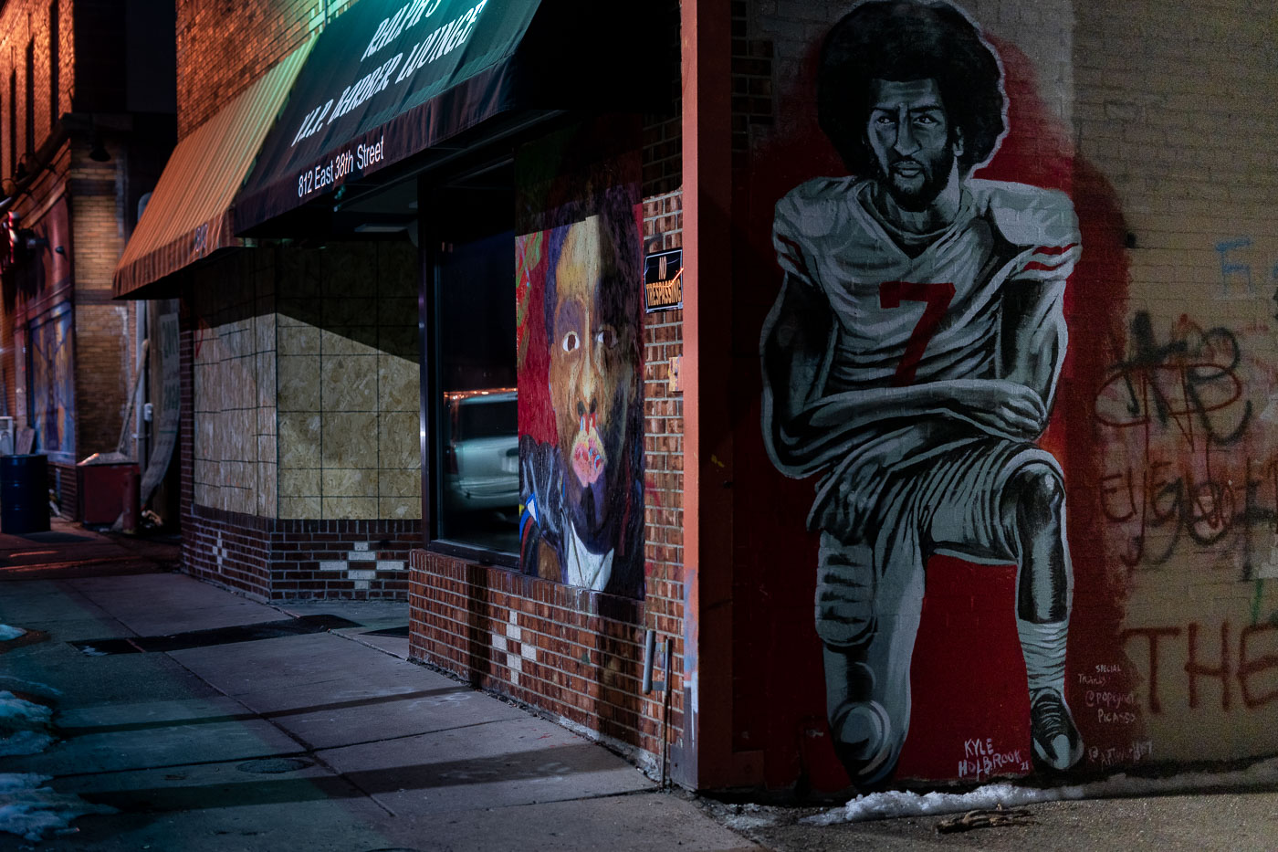 A mural depicting former NFL quarterback Colin Kaepernick kneeling is displayed on the exterior of a building at 812 East 38th Street in Minneapolis. The artwork is situated near George Floyd Square, a location that became a significant site of protest and activism following the murder of George Floyd in May 2020. Kaepernick, known for his protests against racial injustice and police brutality during NFL games, is honored in this mural, which serves as a visual statement within a neighborhood that has been central to discussions on racial equality and social justice.