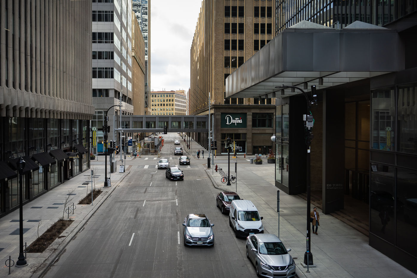 Nicollet Mall and 8th Street in Downtown Minneapolis, Minnesota, are shown with the IDS Center and the former Dayton's department store building. Nicollet Mall, originally a street, was redeveloped into a pedestrian mall in the 1960s to revitalize the downtown core and encourage foot traffic. The IDS Center, completed in 1973, became a landmark of the city's central business district. The skywalk system, visible connecting buildings, was developed to provide weather-protected pedestrian access throughout downtown Minneapolis, enhancing its functionality.