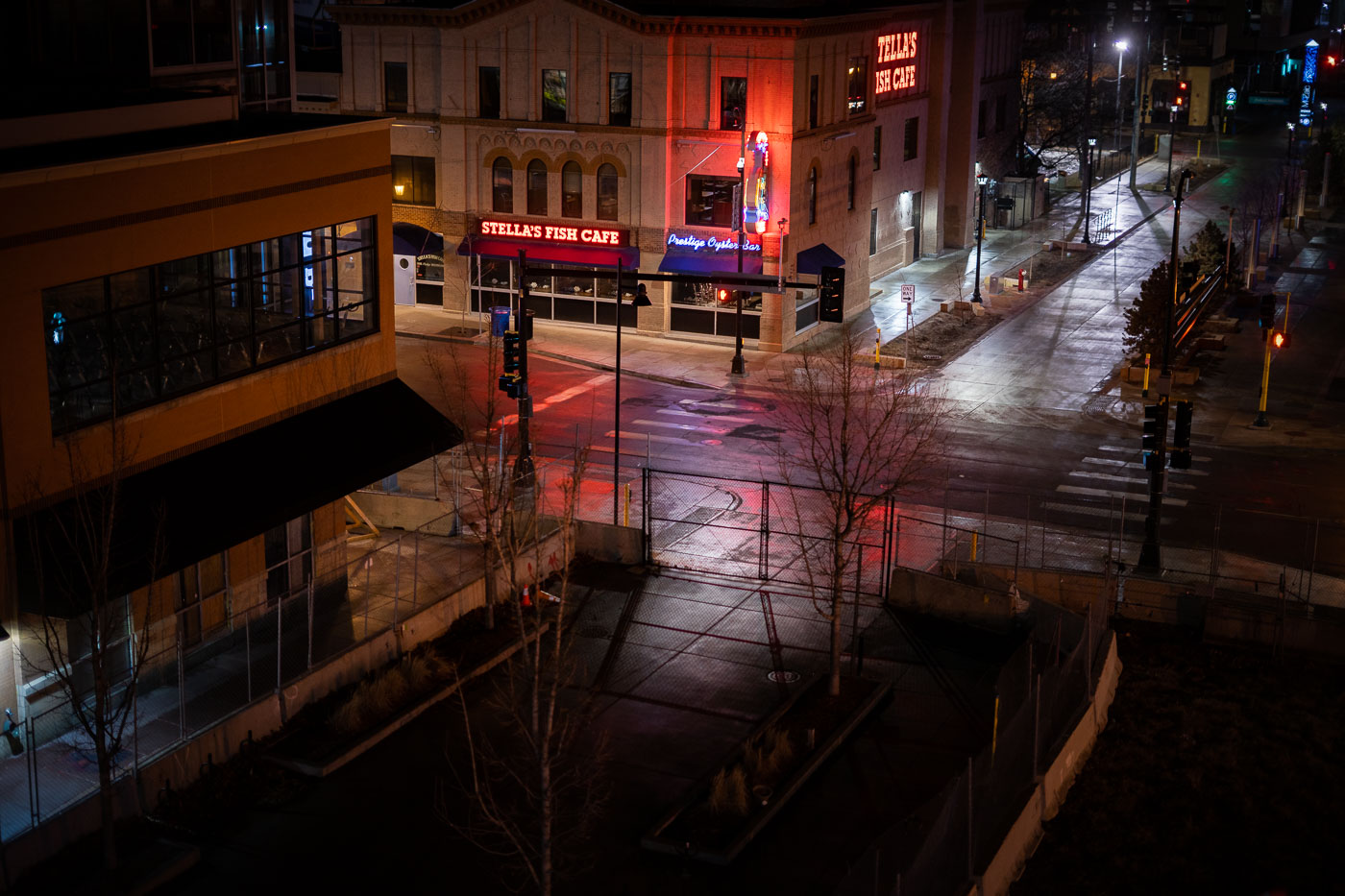 The intersection of Lake Street and Girard Avenue in Uptown Minneapolis is shown at night. This area was a focal point during the 2020 Minneapolis uprising, following the murder of George Floyd. The buildings visible include Stella's Fish Cafe, a long-standing establishment in the neighborhood, and the Seven Points Mall, which also experienced significant damage and activity during the unrest. The photograph captures the streetscape after dark, with illuminated signs and traffic signals reflecting on the wet pavement, hinting at the recent events that have impacted this urban environment.