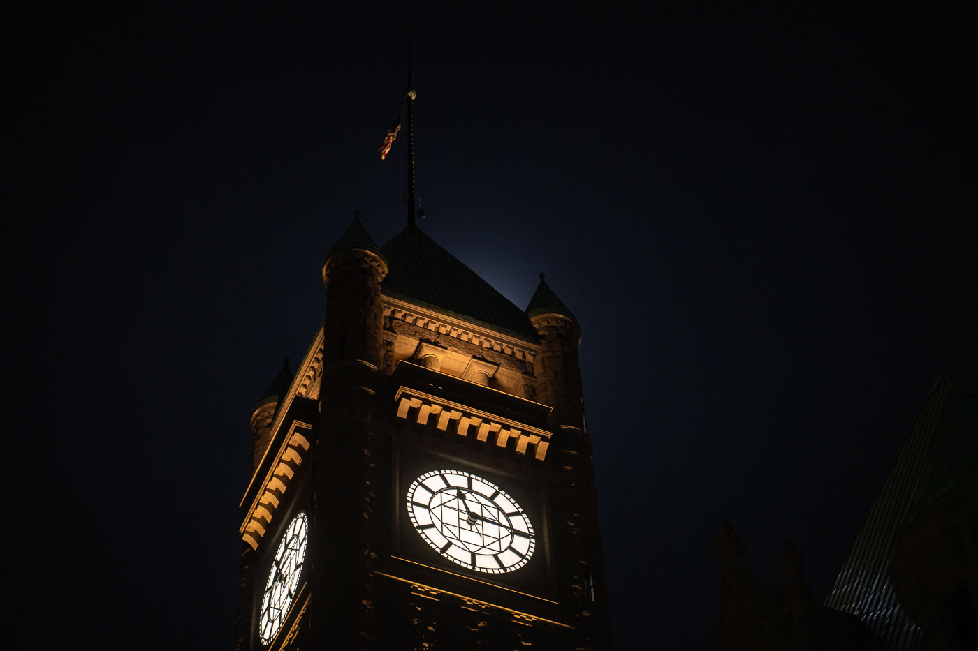 The Minneapolis City Hall Clock Tower, a Beaux-Arts structure completed in 1909, is illuminated at night. This building has served as the seat of Minneapolis city government for over a century and remains a prominent landmark. The tower's clock faces are visible against the dark sky, highlighting its architectural significance. The building has been a backdrop to significant historical moments, including protests in downtown Minneapolis in 2020.