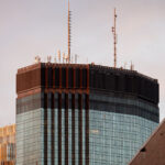 The IDS Center rises into the evening light in downtown Minneapolis, its rooftop antennas silhouetted against a soft autumn sky. Designed by Philip Johnson and John Burgee and completed in 1972, the 792-foot tower remains the tallest building in Minnesota. The dark mechanical crown houses HVAC systems and broadcast transmitters, while the curtain wall’s reflective glass panels catch the last warm tones of sunset alongside the adjacent RBC Gateway Tower.