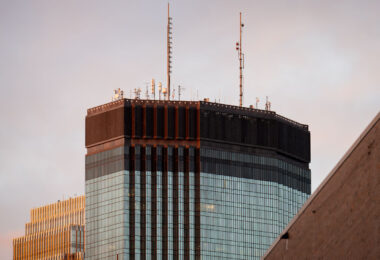 The IDS Center rises into the evening light in downtown Minneapolis, its rooftop antennas silhouetted against a soft autumn sky. Designed by Philip Johnson and John Burgee and completed in 1972, the 792-foot tower remains the tallest building in Minnesota. The dark mechanical crown houses HVAC systems and broadcast transmitters, while the curtain wall’s reflective glass panels catch the last warm tones of sunset alongside the adjacent RBC Gateway Tower.
