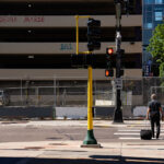 A couple walk across Lake Street in front of a parking garage with graffiti that reads “Deona Marie” “161”. The area has been a place of protest since the June 2021 killing of Winston Smith.Smith was killed by a federal task force serving a warrant. Protester Deona Marie was killed ten days later when a man drove his vehicle through barricades killing her.