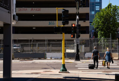 A couple walk across Lake Street in front of a parking garage with graffiti that reads “Deona Marie” “161”. The area has been a place of protest since the June 2021 killing of Winston Smith.

Smith was killed by a federal task force serving a warrant. Protester Deona Marie was killed ten days later when a man drove his vehicle through barricades killing her.